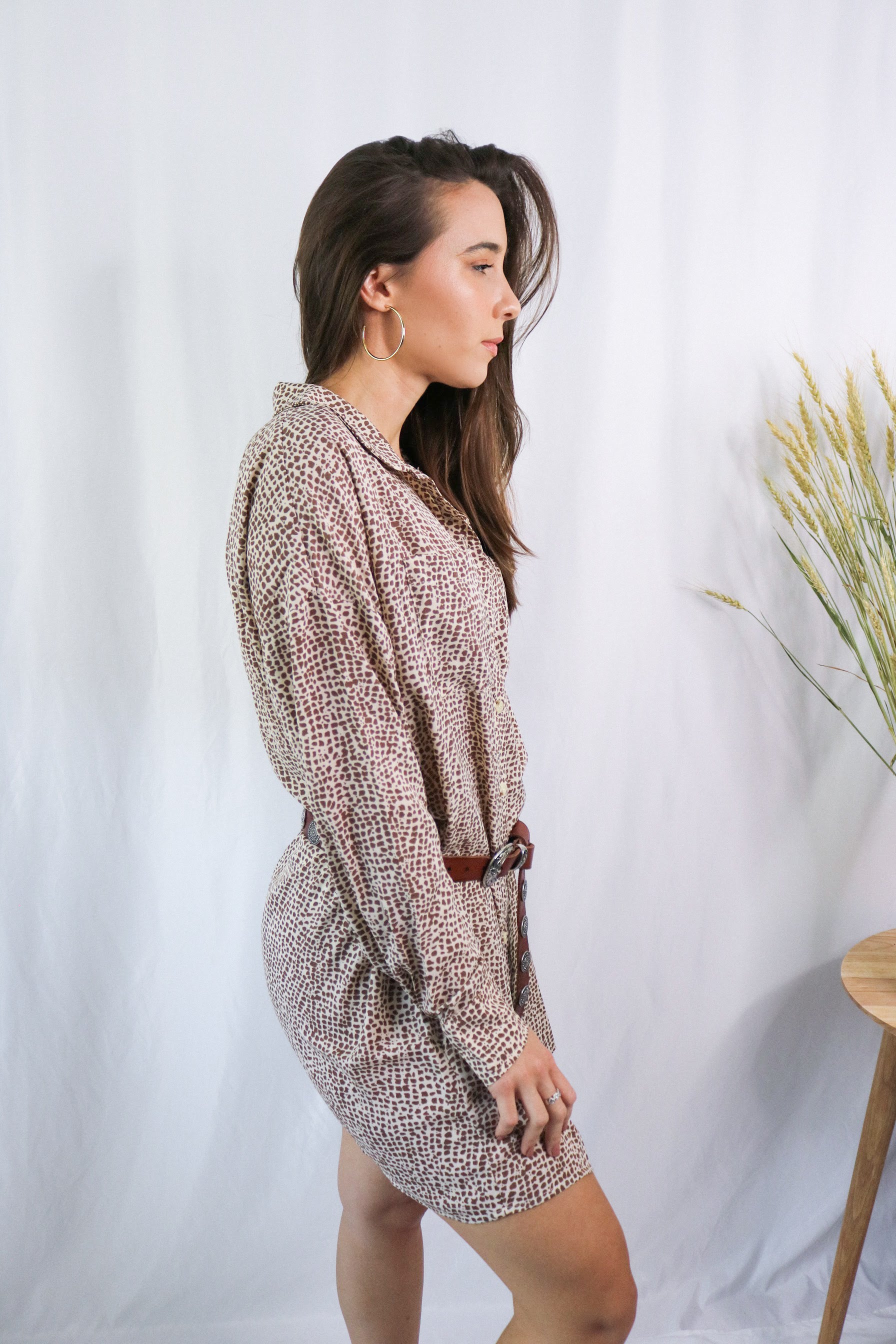 Brunette girl models a collared T-Shirt Dress in Animal Print (cheetah / leopard print). The t-shirt dress is collared, brown, and mid-length. It is a long sleeve t-shirt dress with a loose and comfortable fit and paired with a brown belt.