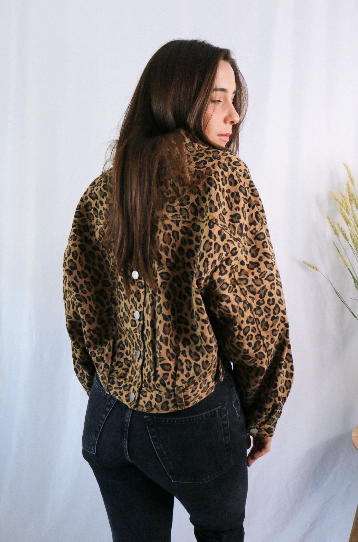 Brunette girl models a buttoned leopard jacket for Scarlette The Label, an online fashion boutique for women. Paired with white ribbed spaghetti strap tank top in white and dark denim jeans.