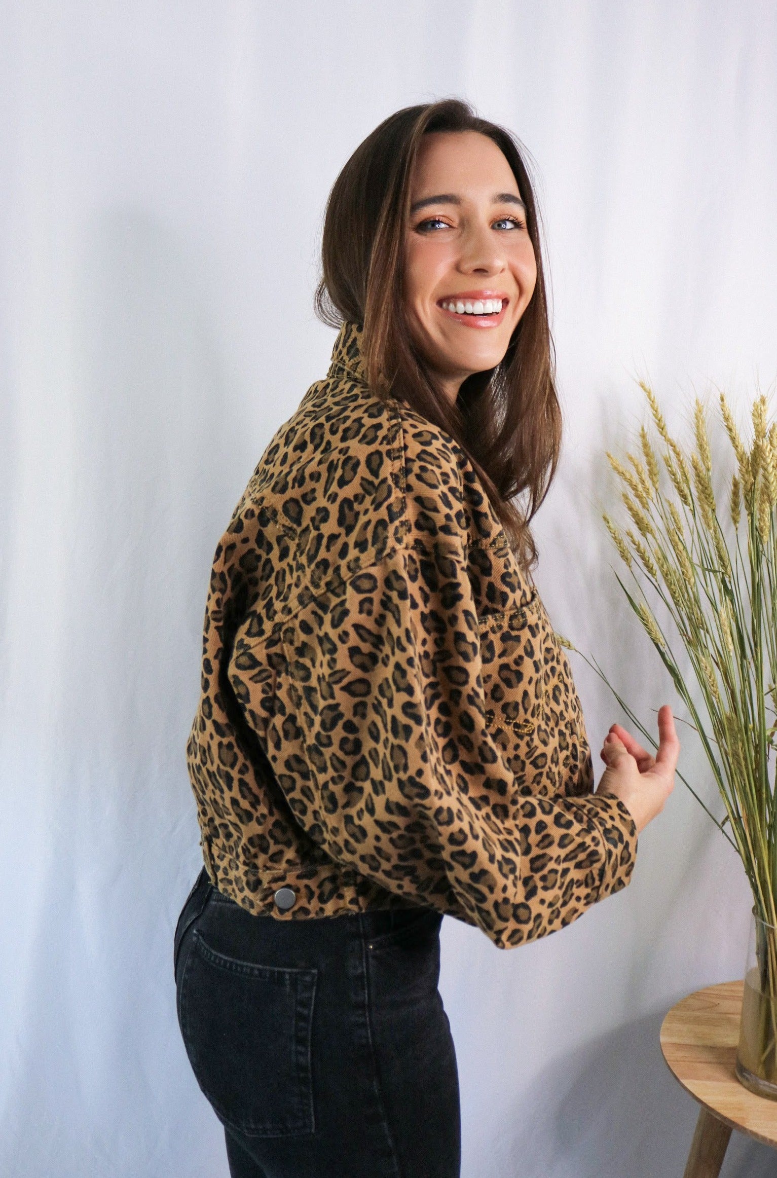 Brunette girl models a buttoned leopard jacket for Scarlette The Label, an online fashion boutique for women. Paired with white ribbed spaghetti strap tank top in white and dark denim jeans.