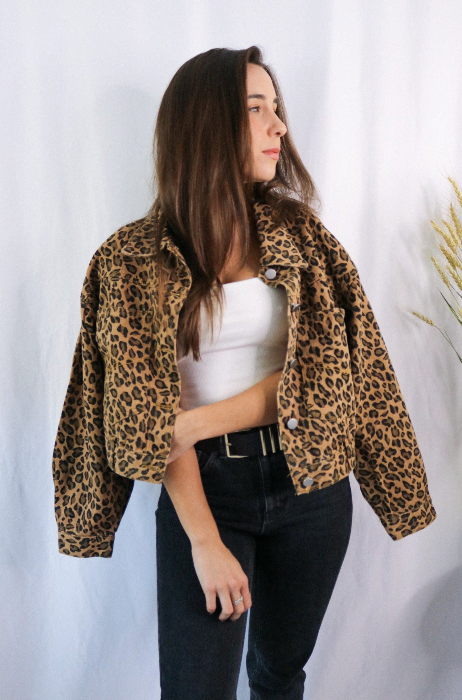 Brunette girl models a buttoned leopard jacket for Scarlette The Label, an online fashion boutique for women. Paired with white ribbed spaghetti strap tank top in white and dark denim jeans.