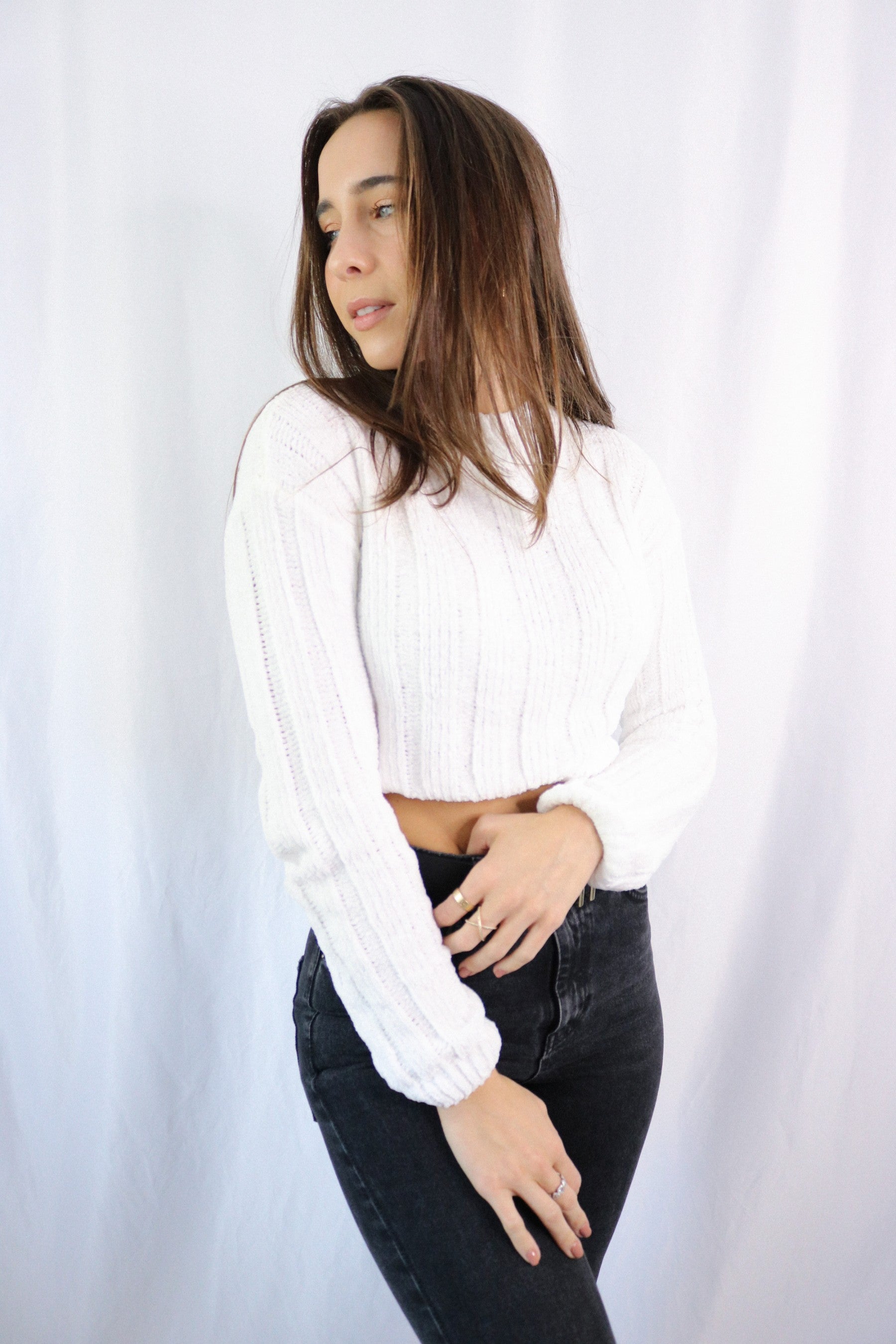 Brunette girl models ivory (white) knitted crop sweater for Scarlette The Label, an online fashion boutique for women. THe knitted crop sweater is very soft and breathable. Paired with dark denim jeans.