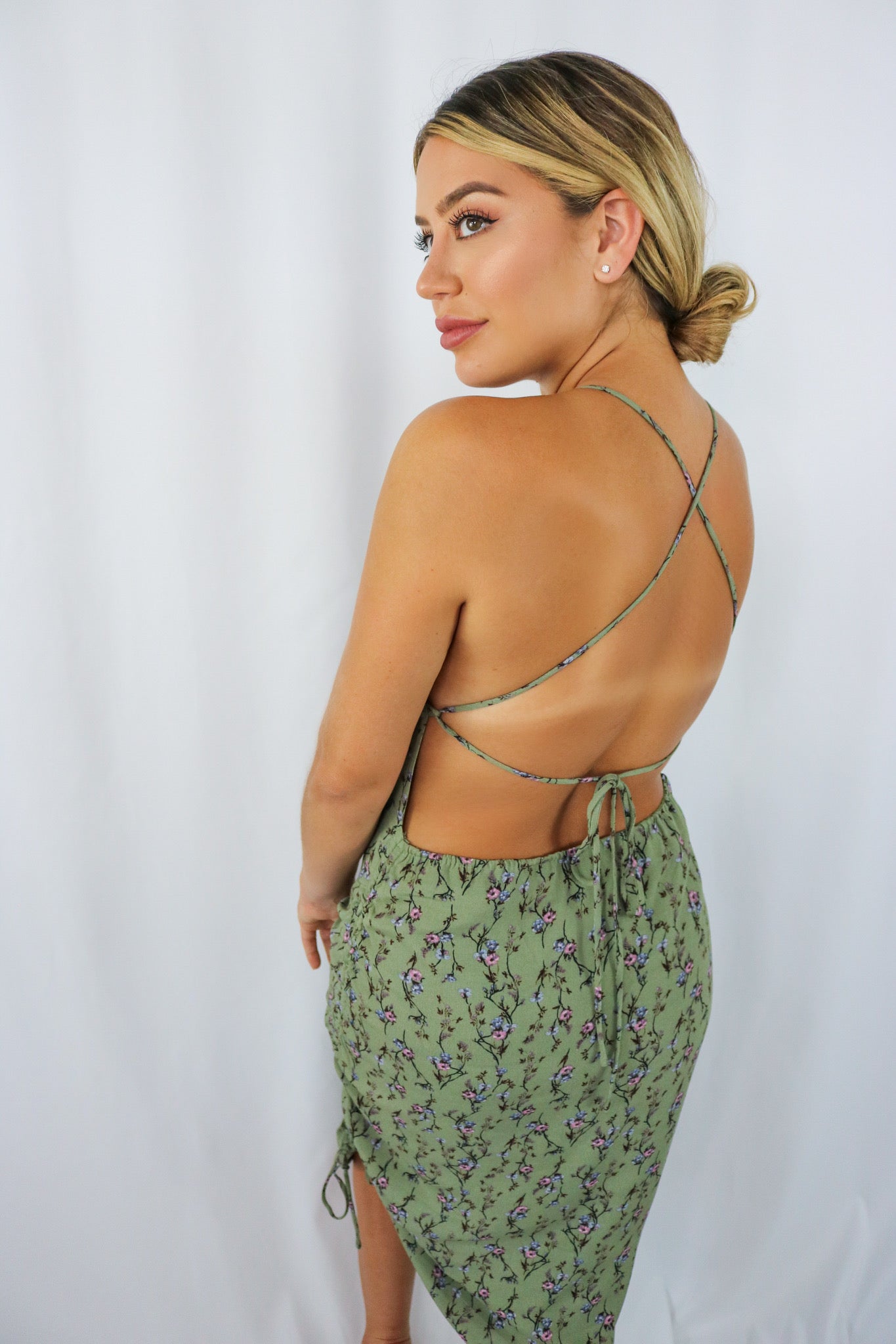 Blonde girl models a green crossback mini dress for Scarlette The Label, an online fashion boutique for women. The mini dress is a scrunched mini dress with floral details, spaghetti straps, and a plunging crossback design in the back.