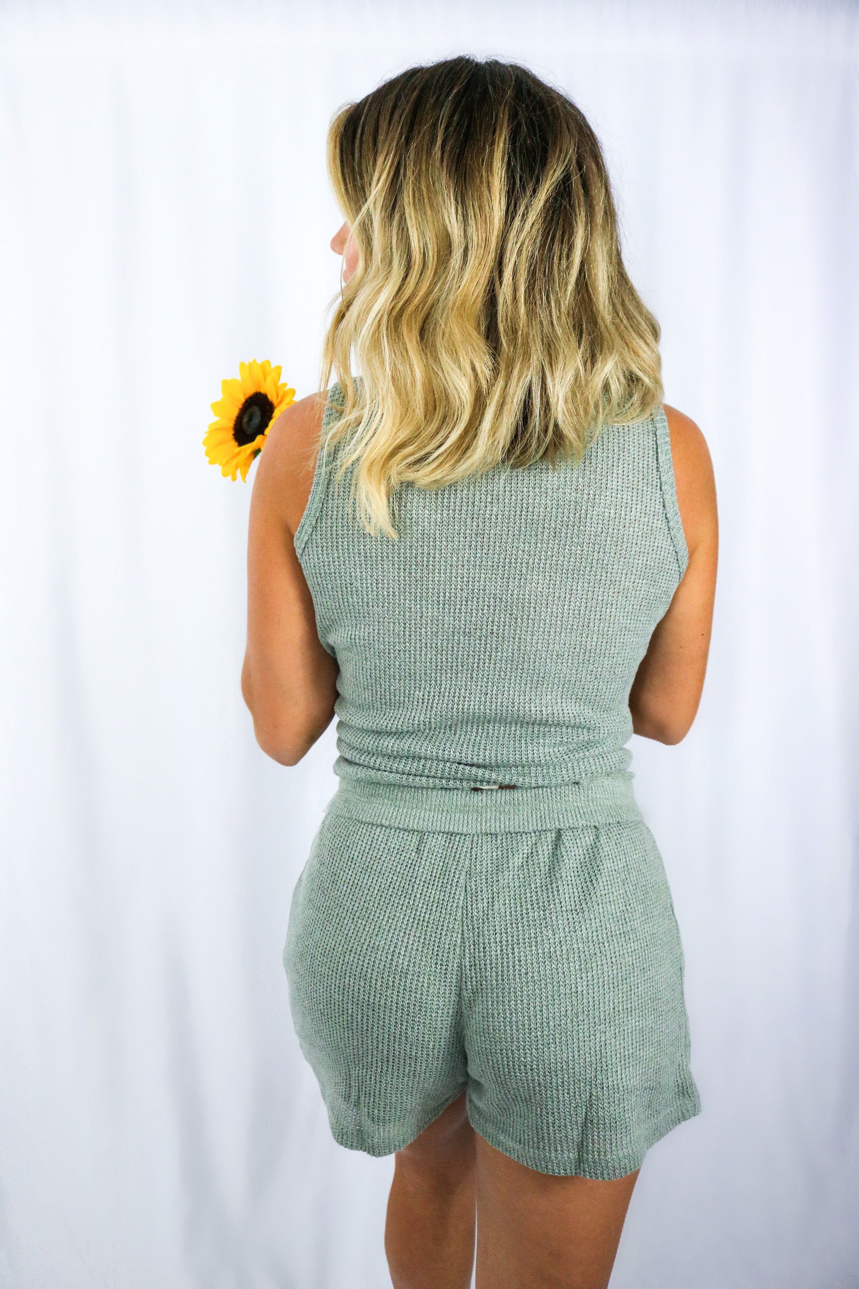 Blonde girl models knitted loungewear short set in color olive for Scarlette The Label, an online fashion boutique for women.