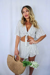 Blonde girl models a matching set for Scarlette The Label, an online fashion boutique for women. The set is a matching short set in white and charcoal stripes. Includes a short sleeve tie top and a skort. Paired with large straw bag.