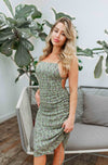 Blonde girl models a green crossback mini dress for Scarlette The Label, an online fashion boutique for women. The mini dress is a scrunched mini dress with floral details, spaghetti straps, and a plunging crossback design in the back.