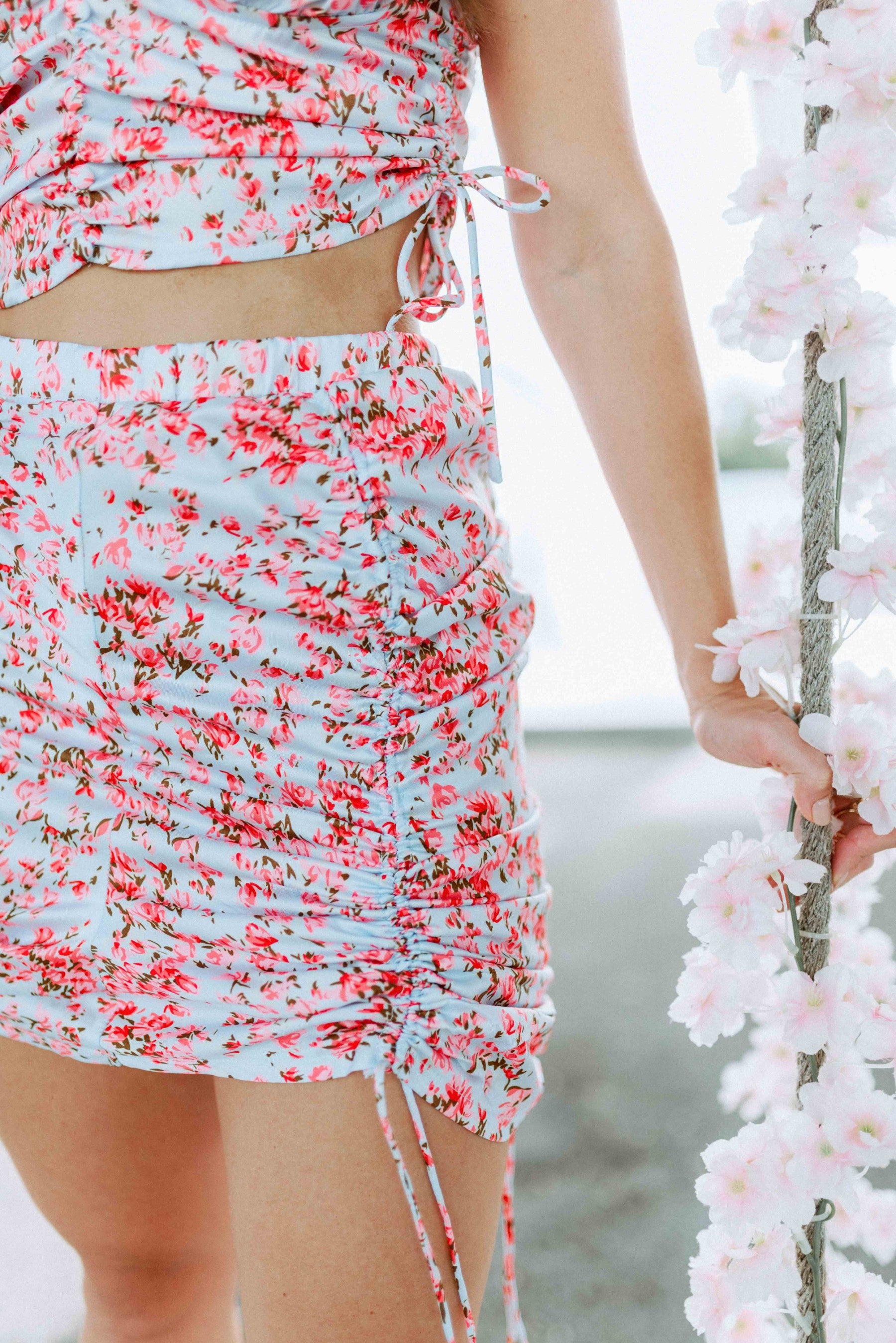 Brunette modeling a floral print matching mini scrunch skirt set in light blue and pink for Scarlette The Label, an online fashion boutique for women.