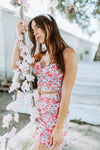 Brunette modeling a floral print matching mini scrunch skirt set in light blue and pink for Scarlette The Label, an online fashion boutique for women.